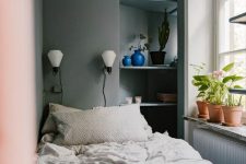 a narrow bedroom in greys, built-in shelves, potted plants and blooms, a bed with neutral bedding and sconces