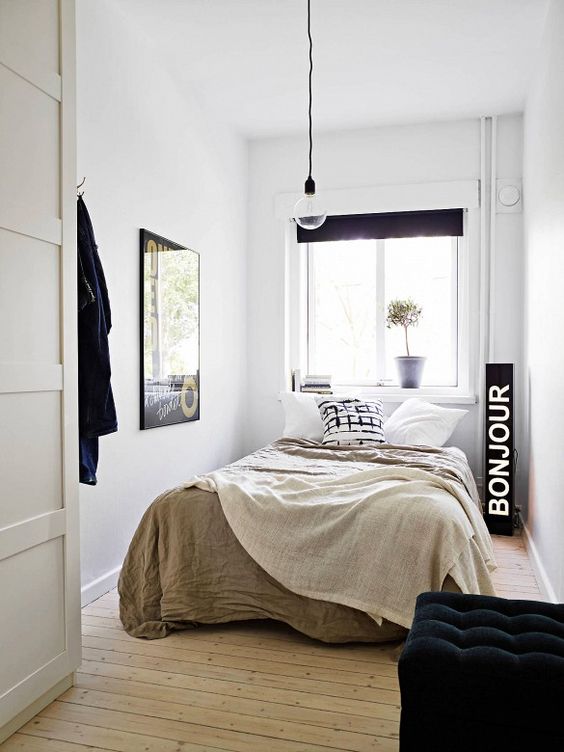 a narrow bedroom in neutrals and black, with a black sign, a pendant lamp and a black pouf is a cool idea