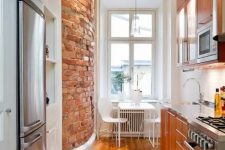 a narrow kitchen with rich-stained cabinets, built-in appliances, a brick wall, a white dining set and a stained floor
