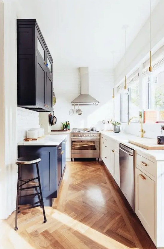 a narrow kitchen with white and navy shaker style cabinets, white stone countertops and a lot of natural light coming through the windows