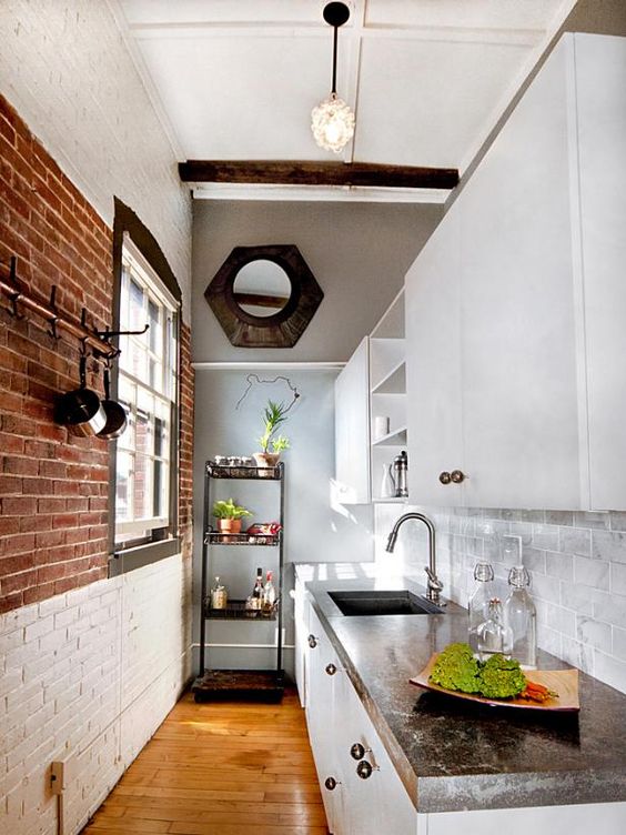 a narrow modern kitchen with brick walls, white cabinetry, stone countertops, open shelvesand pendant lamps