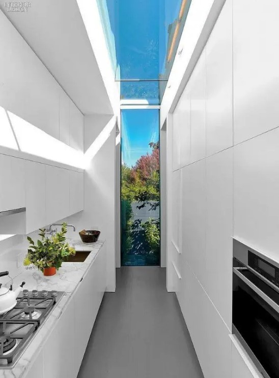 a narrow white kitchen with sleek cabinets, built-in appliances, a skylight going into a window to the garden, for natural light and a view