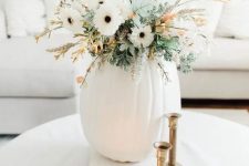 a neutral Thanksgiving centerpiece of a white pumpkin, white blooms, greenery and some blooming branches is cool