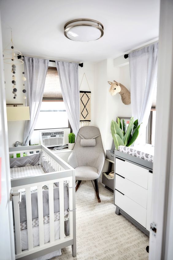 a neutral modern nursery with a grey and white crib, a matching dresser, a grey chair, light grey curtains and some decor