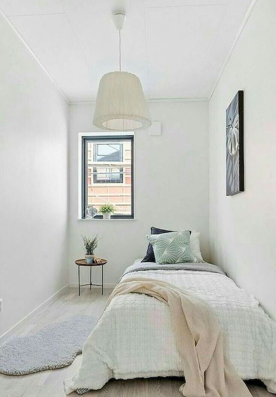 a neutral narrow bedroom with a bed, some art, potted plants and a pendant lamp is a cool guest bedroom