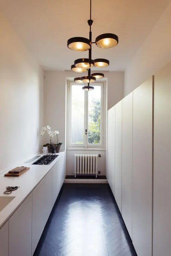 a neutral narrow kitchen with lower cabinets and tall ones on the second wall, eye catching lamps and built in appliances