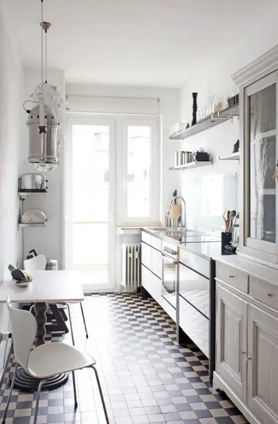 a neutral narrow kitchen with vintage cabinets and open shelving, a checked floor, a table and white chairs and pendant lamps