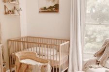 a neutral nursery with a stained crib, a bassinet, a white chair and ottoman, a printed rug, bookshelves and artwork