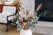 a pretty floral Thanksgiving centerpiece of a white pumpkin, burgundy and white blooms, greenery and dried grass
