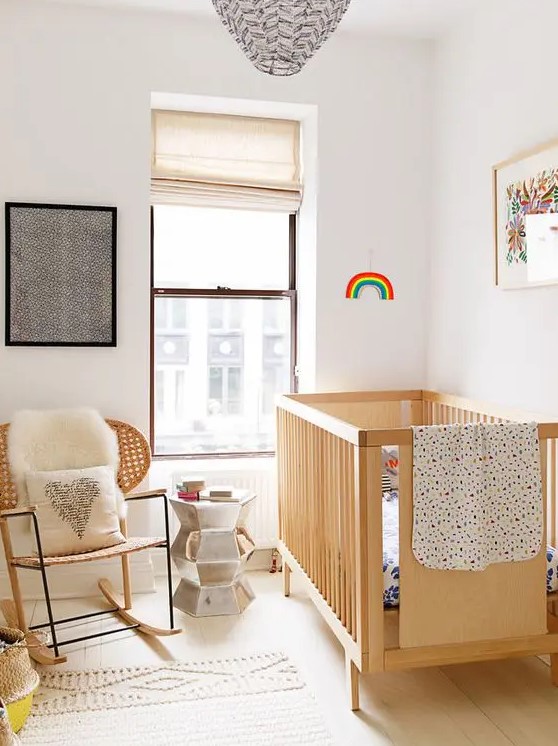 a pretty small nursery with a stained crib and a chair, some art, neutral and printed textiles and a metallic side table