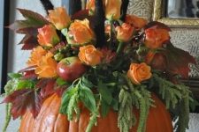 a pumpkin with greenery, faux apples, faux orange blooms and feathers is a stylish fall centerpiece or decoration