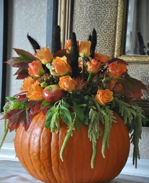 a pumpkin with greenery, faux apples, faux orange blooms and feathers is a stylish fall centerpiece or decoration