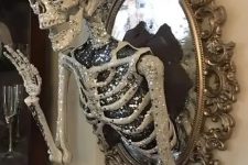 a scary glam Halloween decoration of a vintage mirror with a glam embellished half skeleton attached is elegant