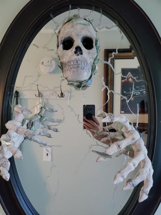 a skeleton mirror with a skull and skeleton hands is a cool and pretty decor idea for Halloween