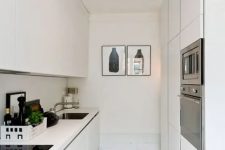 a sleek narrow white kitchen with minimalist cabinetry, built-in appliances and some artwork is amazing
