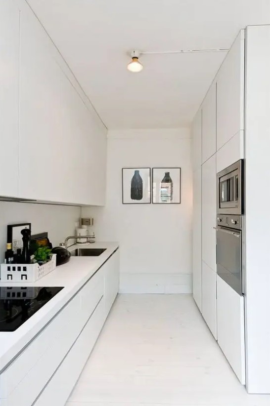 a sleek narrow white kitchen with minimalist cabinetry, built in appliances and some artwork is amazing