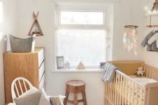 a small Scandinavian nursery with a light-stained crib, a white rocker chair with pillows, a dresser, a stool and some lovely decor