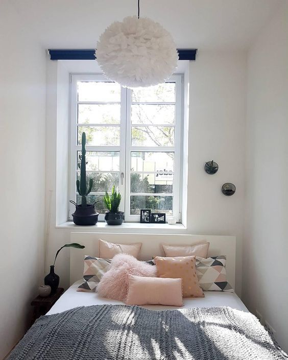 a small and narrow bedroom with a white bed, pink and printed bedding, a single nightstand and some potted plants