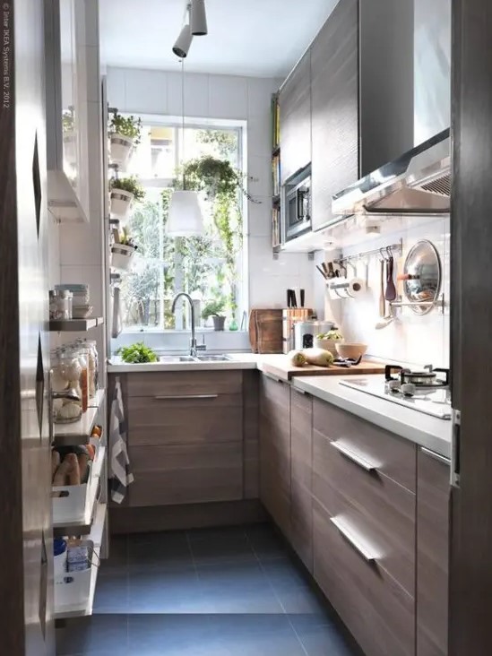 a small and narrow galley kitchen with white stone countertops, potted herbs and some open shelving