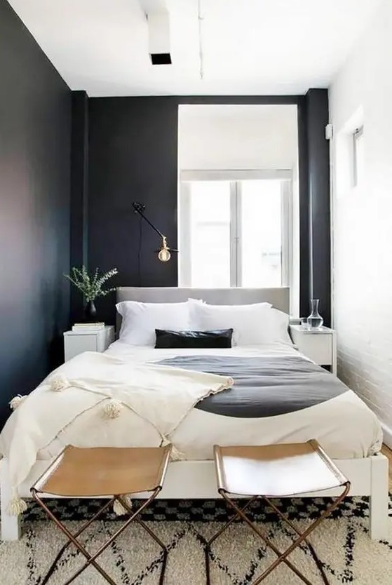 a small and narrow modern bedroom with black and white walls, a neutral bed with catchy bedding, leather stools