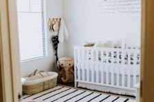 a small boho nursery with layered rugs, a white crib with printed bedding, a leather pouf, tassel chandelier and lovely decor