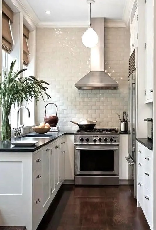 a small narrow kitchen with glazed white tiles, shaker cabinets, black countertops, pendant lamps and shades