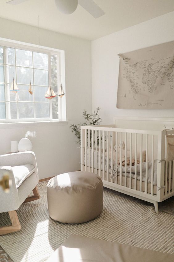a small neutral nursery with a crib, a rocker chair, a grey pouf, layered rugs and some pretty decor is very welcoming