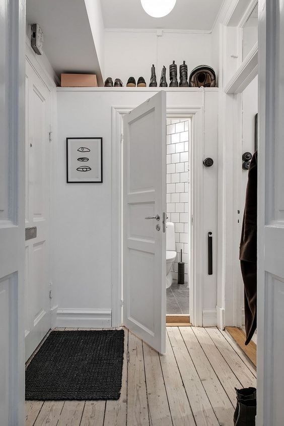 a small white entryway with a shelf over the doorway to store boots and shoes is a smart and cool idea to organize a space