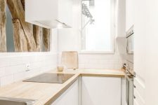 a small white minimalist U-shaped kitchen with butcherblock countertops, white subway tiles and rough wood for deocr
