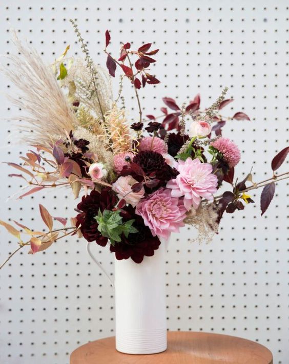 a sophisticated faux flower arrangement in burgundy and pink, grasses and dark foliage is an amazing centerpiece