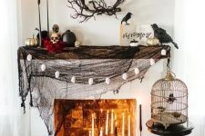 a stylish Halloween mantel with black spiderweb, lots of candles, skulls and black and gilded pumpkins plus blackbirds
