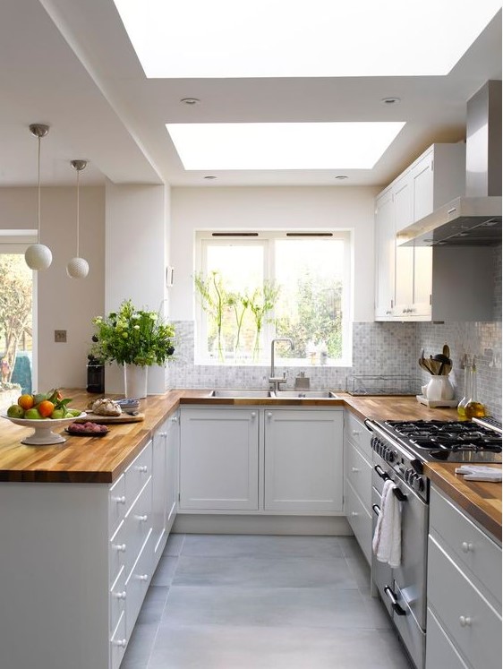 a stylish U-shaped kitchen in white, with only lower cabinets and butcherblock countertops, skylights and pendant sphere lamps