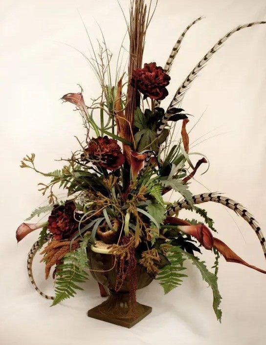 a stylish fall centerpiece of a vintage urn, greenery, feathers and faux blooms is an elegant boho-inspired decoration to make for fall
