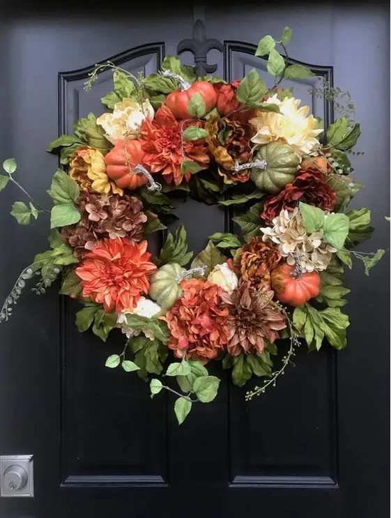 a stylish fall wreath of greenery, faux pumpkins and bright blooms is a cool decoration to rock