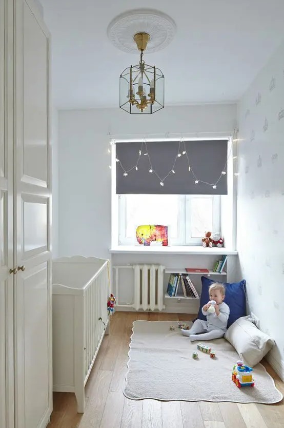 a tiny nursery with a white vintage crib, a windowsill as a table, some bookshelves and a play space on the floor