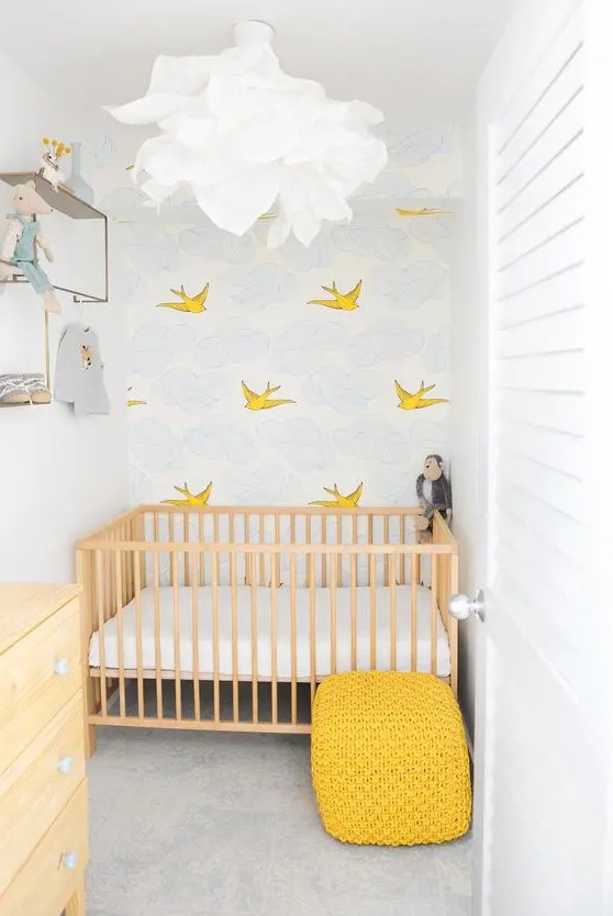 a tiny nursery with an accent wall, a stained crib with neutral bedding, a stained dresser, a yellow pouf and some shelves