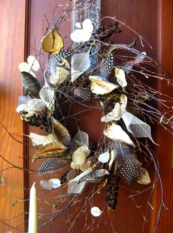 a twig fall wreath with dried leaves, blooms, feathers and berries looks boho-like and woodland-inspired