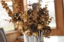 a vase covered with silver painted sticks and twigs, dried eucalyptus and pinecones is a chic fall centerpiece