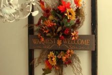 a vintage-inspired faux flower decoration with twigs, grasses and leaves in a frame and with a sign
