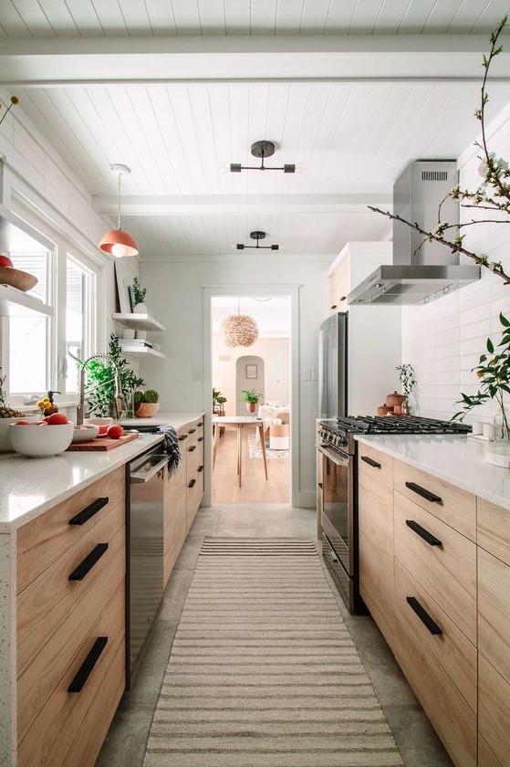a welcoming light-stained galley kitchen with white countertops and a tile backsplash, with potted greenery and pendant lamps