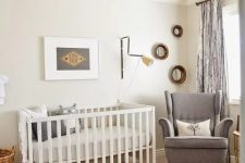 a welcoming mid-century modern nursery in neutrals, with a white crib, a grey rocker chair, layered rugs, a leather pouf and some artwork