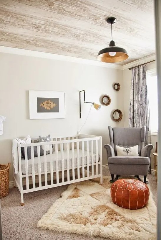 a welcoming mid-century modern nursery in neutrals, with a white crib, a grey rocker chair, layered rugs, a leather pouf and some artwork