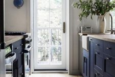 a welcoming navy farmhouse kitchen with navy cabinets and wooden countertops, with a wooden floor and much natural light from the door