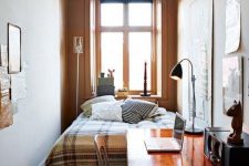 a welcoming small bedroom with a bed and printed bedding, a stained desk and a chair, a table lamp, a gallery wall