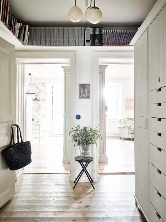 a white Scandinavian entryway with long shelves over the doorways is amazing to store some stuff and display everything you want