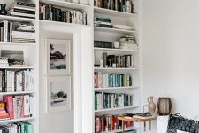 a white Scandinavian living room with a whole doorway wall taken by bookshelves and display shelves to save a lot of space