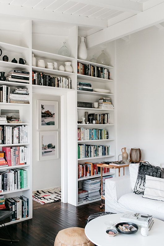 a white Scandinavian living room with a whole doorway wall taken by bookshelves and display shelves to save a lot of space