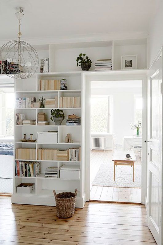 a white entryway with open storage compartments and shelves over the doorways is a cool idea to get more decor and storage space