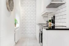 a white kitchen with subway tiles, white cabinets with black countertops, a mirror clock and a whitewashed floor