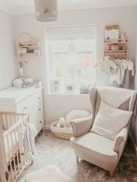 a white nursery with a white dresser, a stained crib, a neutral chair, bookshelves, a makeshift closet and some decor